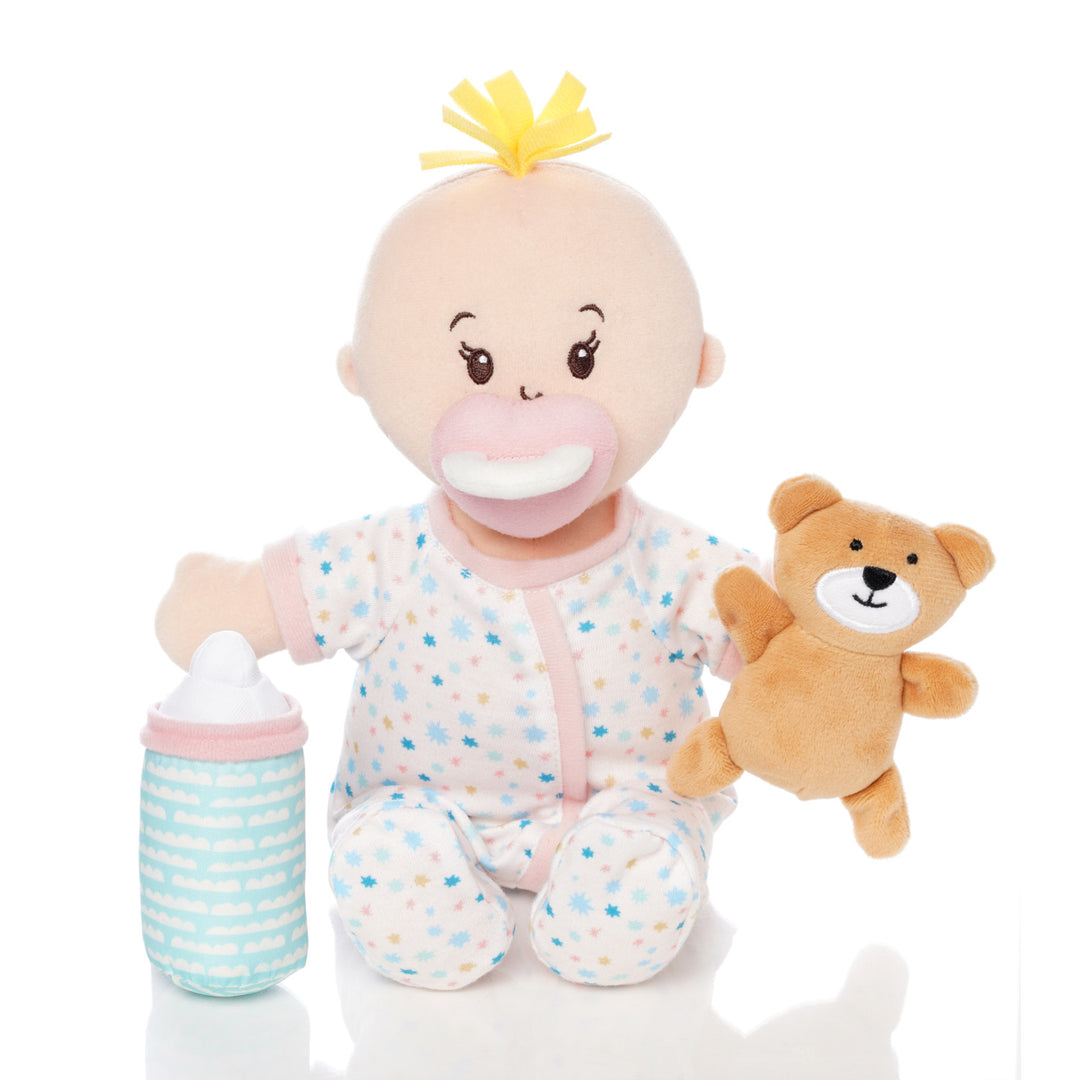 soft doll with peach skin dressed in pjs that comes with a stuffed teddy bear, baby bottle and mini paper picture book doll is seated holding teddy and bottle with magnetic pacifier on face