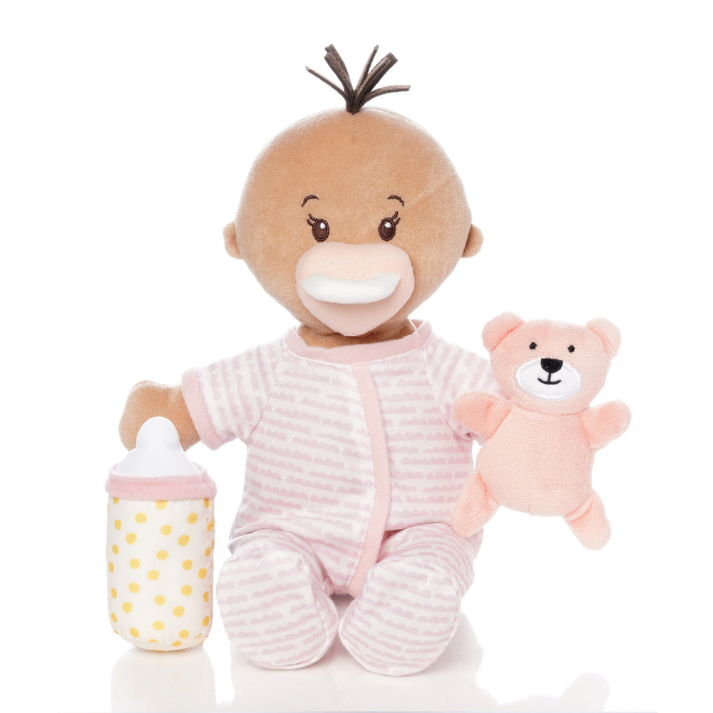 soft doll with beige skin dressed in pjs that comes with a stuffed teddy bear, baby bottle and mini paper picture book doll is seated holding teddy and bottle with magnetic pacifier on face