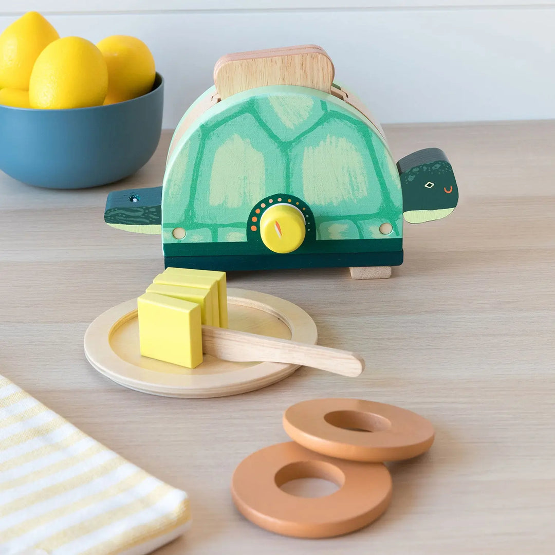 wooden toaster toy that looks like a turtle with slices of toast, butter, plates and bagels