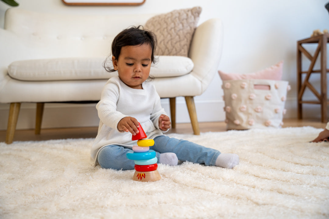 Toddler girl playing with magnetic wood rocket stacker in living room scene