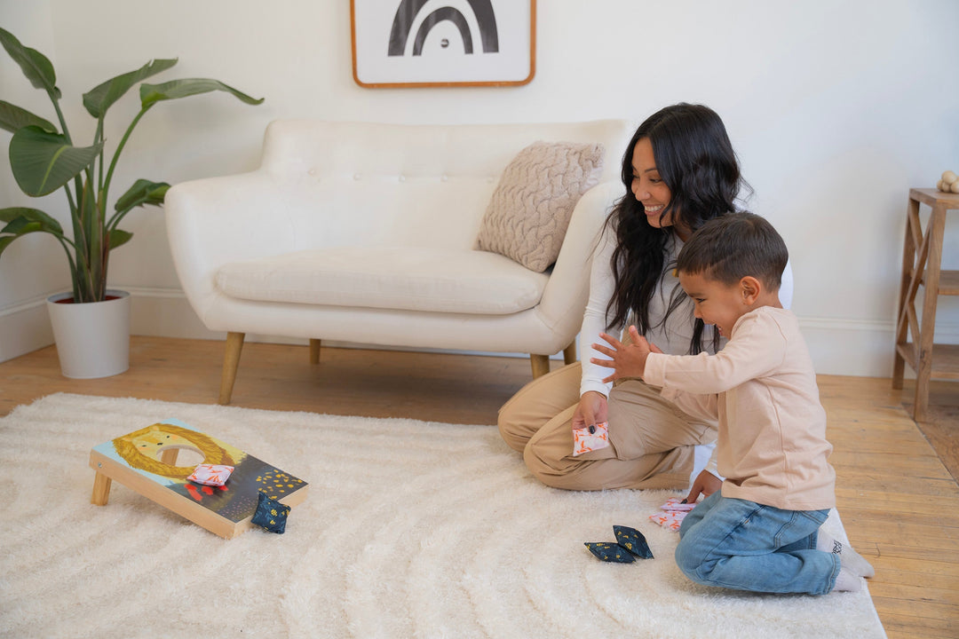 Mom and preschool age son kneeling on the floor in a living room playing a mini corn hole game.