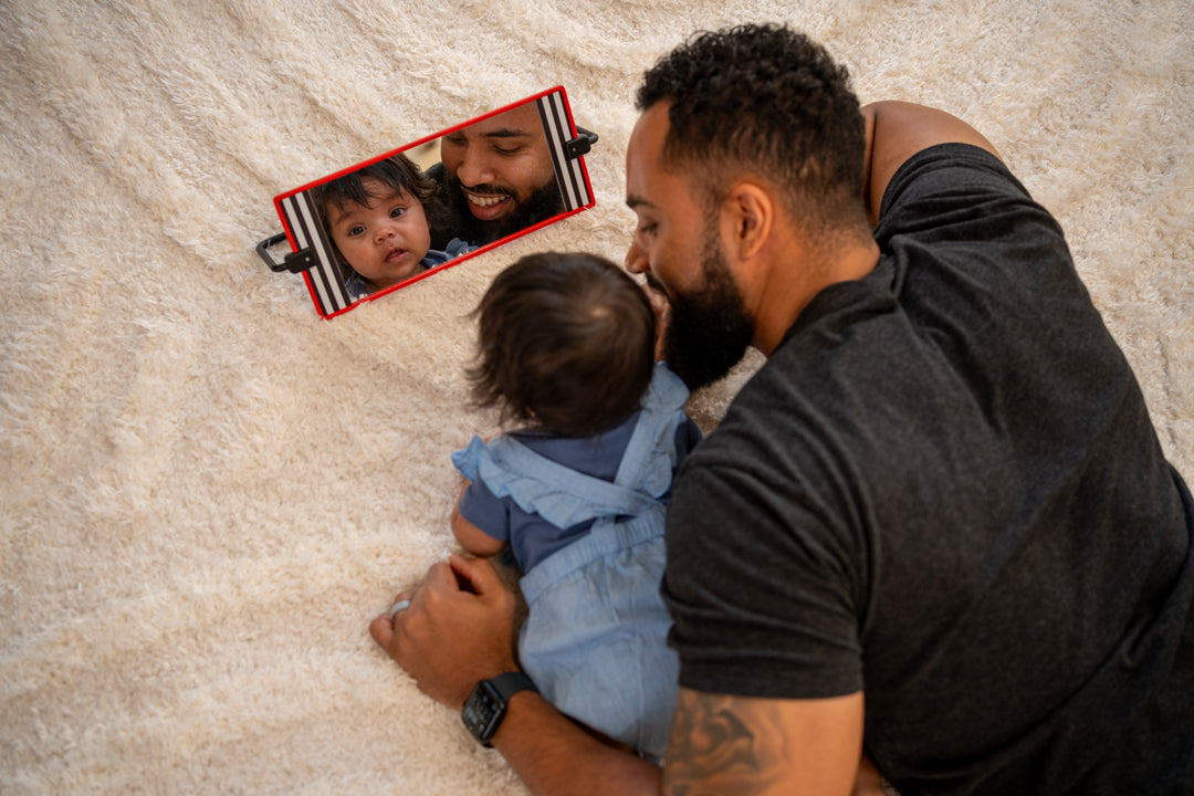 Dad and baby gazing into a mirror while laying on their tummies