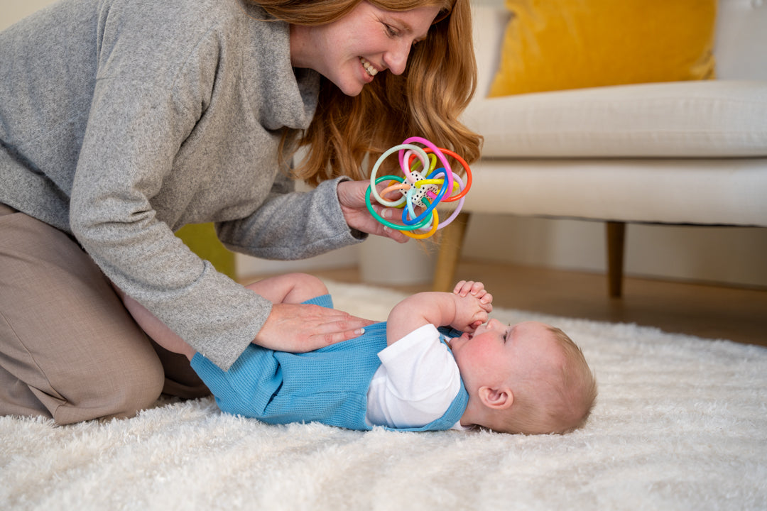 Mom and baby playing with rattle toy on a rug